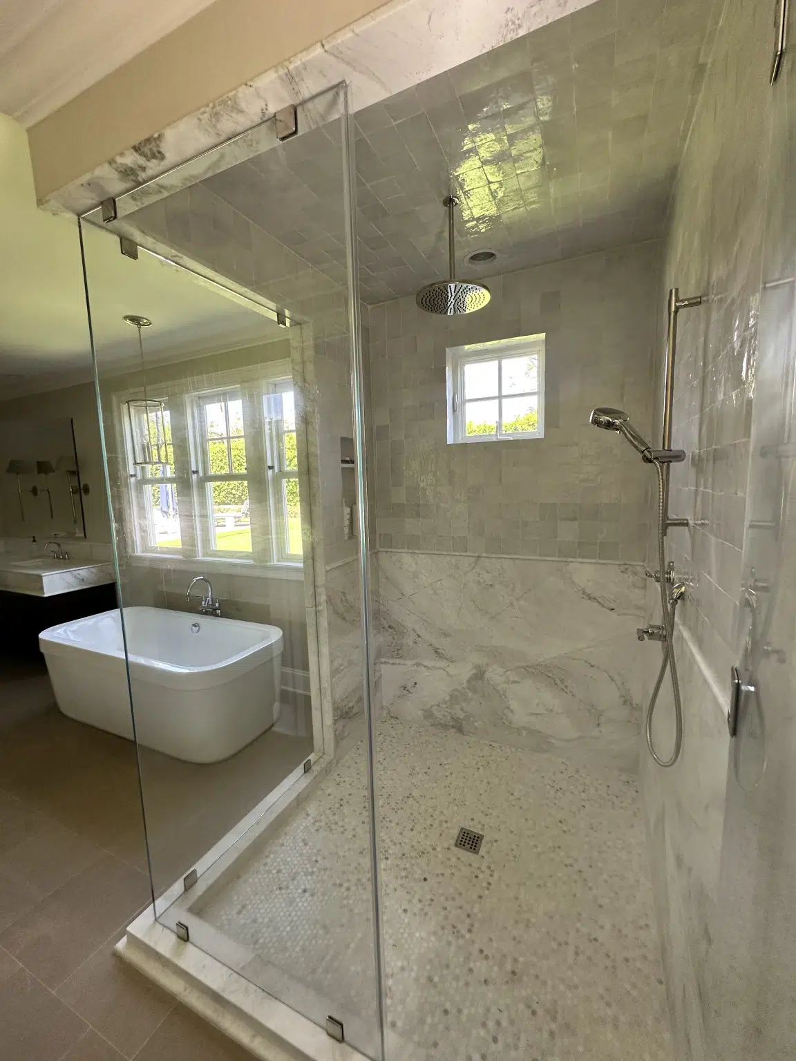 Custom marble shower tile beside a freestanding bathtub suite